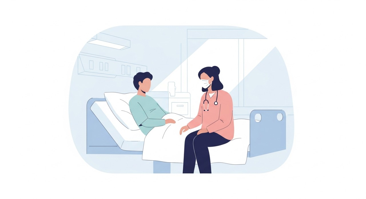 Seorang pelawat duduk di sebelah katil pesakit, berbual perlahan dan beradab sopan di dalam bilik hospital.