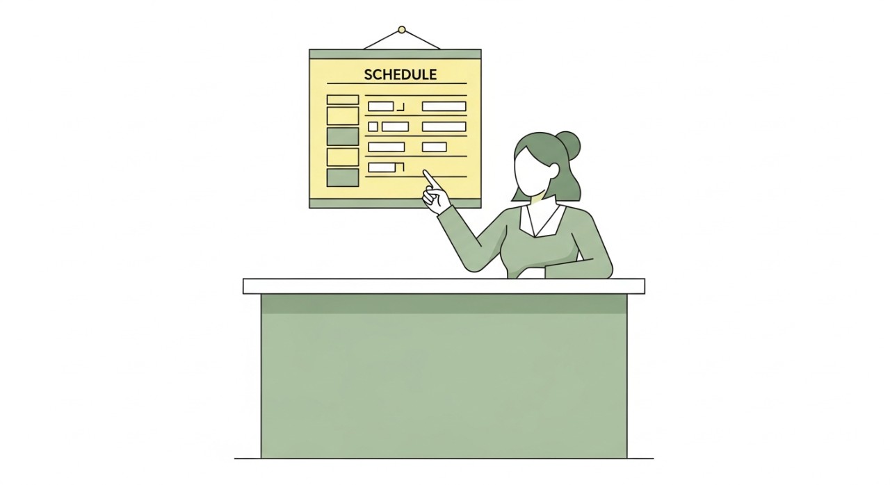 Seorang jururawat sedang menyemak jadual perkhidmatan di kaunter pendaftaran klinik dengan senyuman.